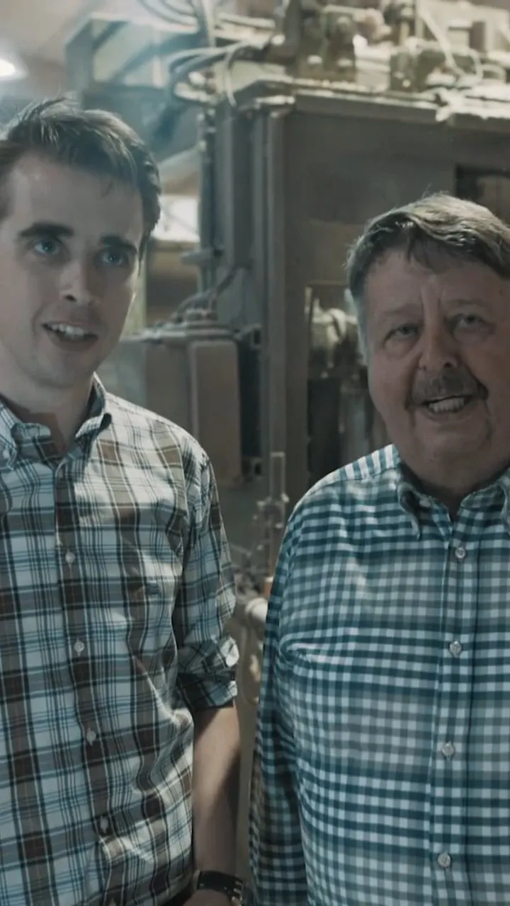 Zwei Männer in karierten Hemden in einer Werkhalle vor Maschinen